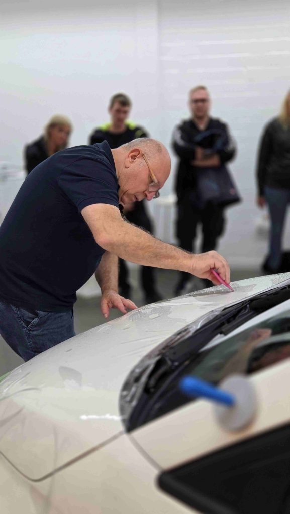 Steinschlagschutzfolie ORAGUARD 2815+ wird von einem Mann mit dem Rakel Pink Squeegee auf einem weißen Auto verklebt.