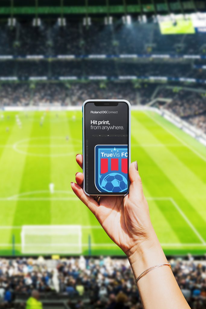 Handy mit Ansicht der Roland DG Connect Software in der Umgebung eines Sportstadions.