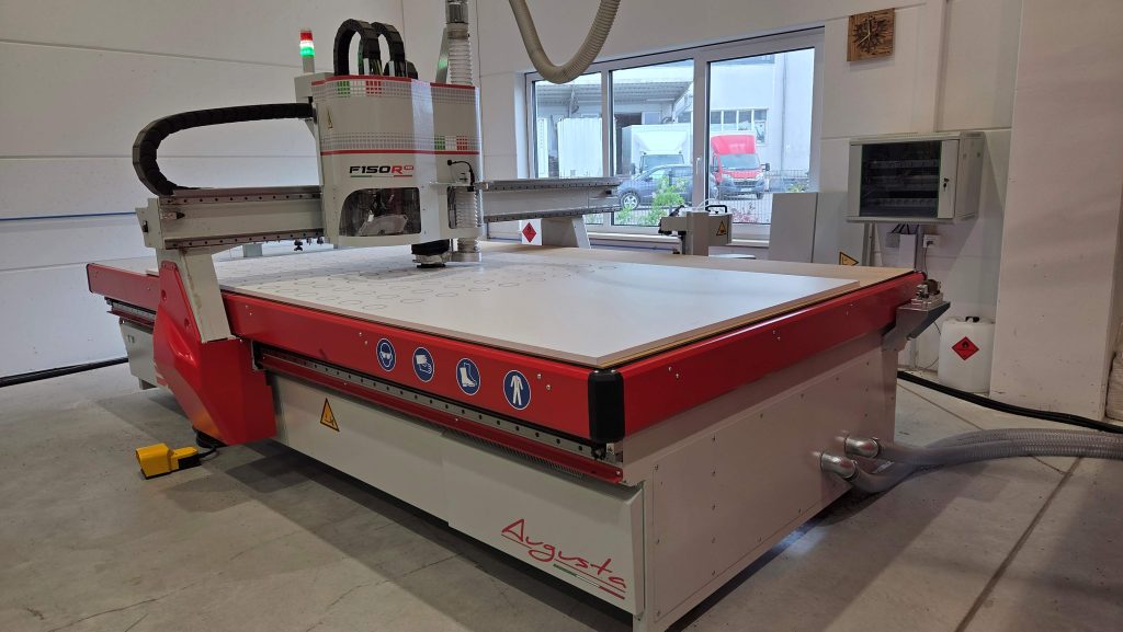 Fräs- und Schneidmaschine F150R Pro von SD Italy mit einer Simopor S-Platte bestückt. Einzelteile einer Baugruppe werden gefräst. Die Hälfte der Platte ist mit Kreisen  bereits gefräst, der Rest ist unbearbeitet.