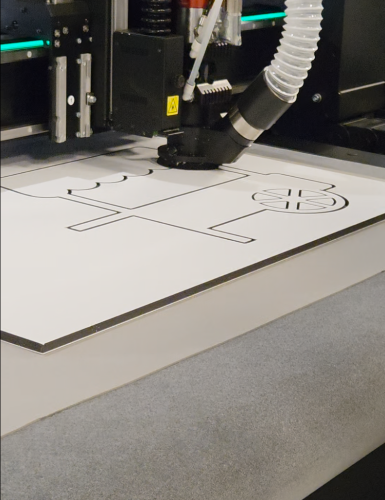 Bearbeitung einer Platte auf dem neuen Flachbett-Schneideplotter F-Serie Vantage. Auf der Platte sind die ersten Schnitte für einen Aufsteller zu sehen. Vermutlich ein Einkaufswagen.