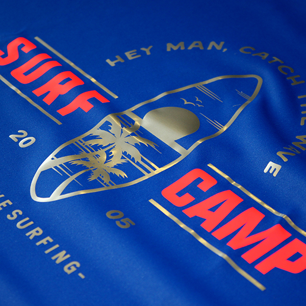 POLI-FLEX® TURBO® als Flexfolie auf einem blauen T-Shirt. Aufschrift "SURF CAMP" in rot, Grafik in gold.