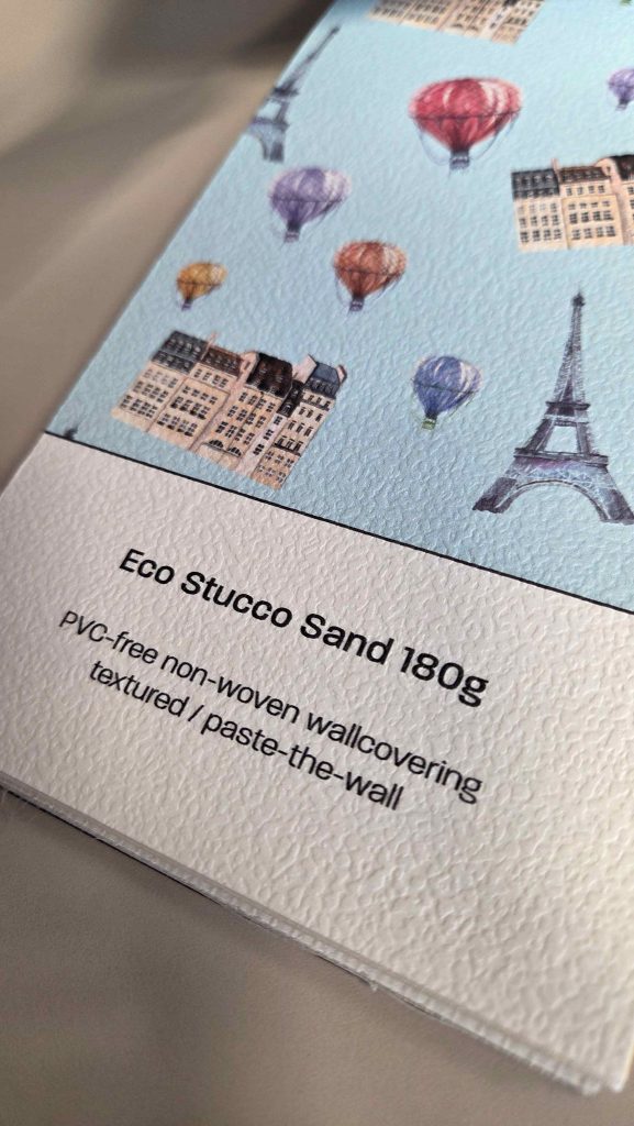 Muster der DESARDI® Eco Stucco Sand 180 g von Farben-Frikell | WTB. Oben sind Häuser, der Eifelturm und Heißluftballons auf einem hellblauen Hintergrund zu sehen.